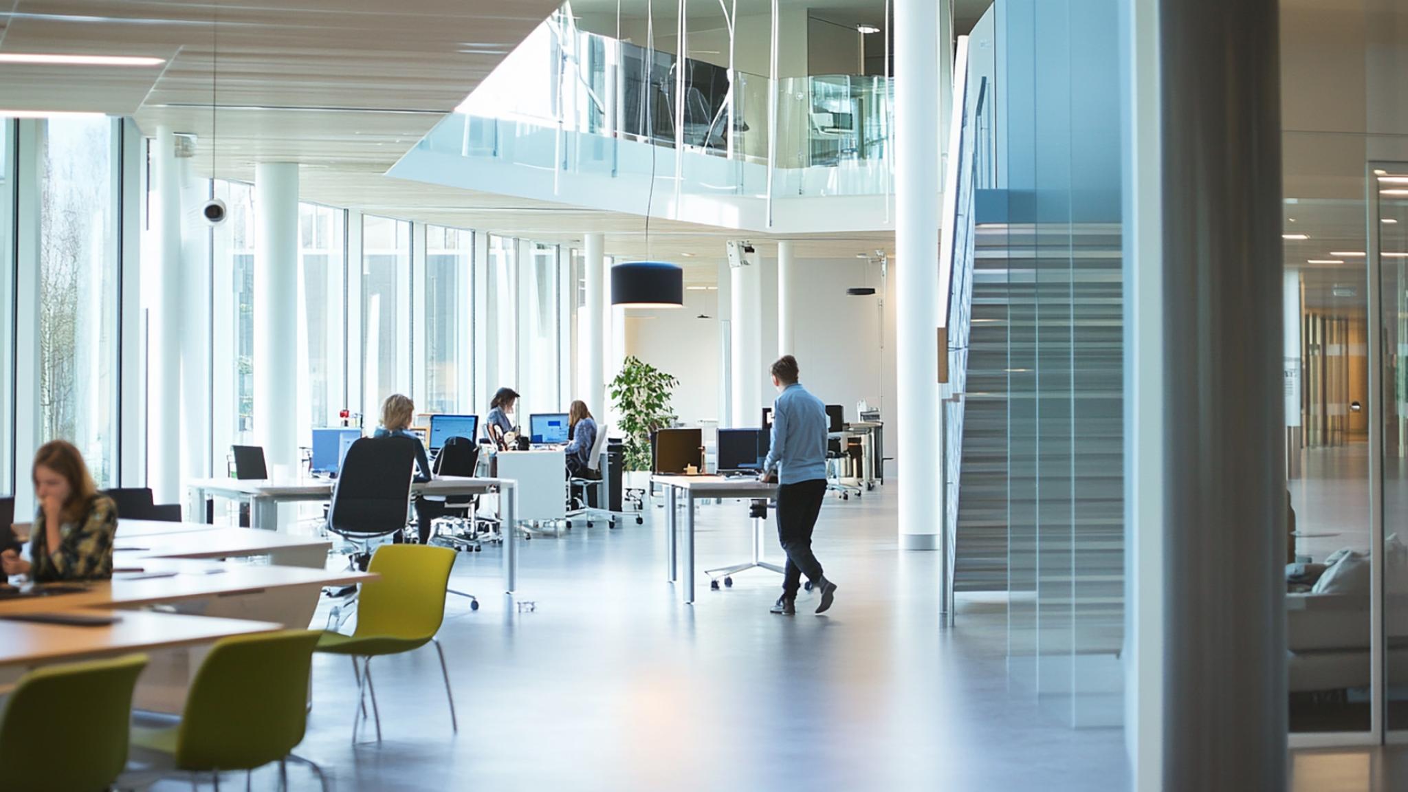 A modern, open-concept office space with large windows, glass partitions, and employees working at desks in a bright and collaborative environment.