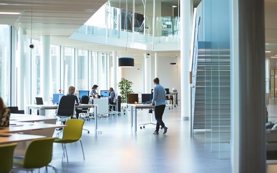 A modern, open-concept office space with large windows, glass partitions, and employees working at desks in a bright and collaborative environment.